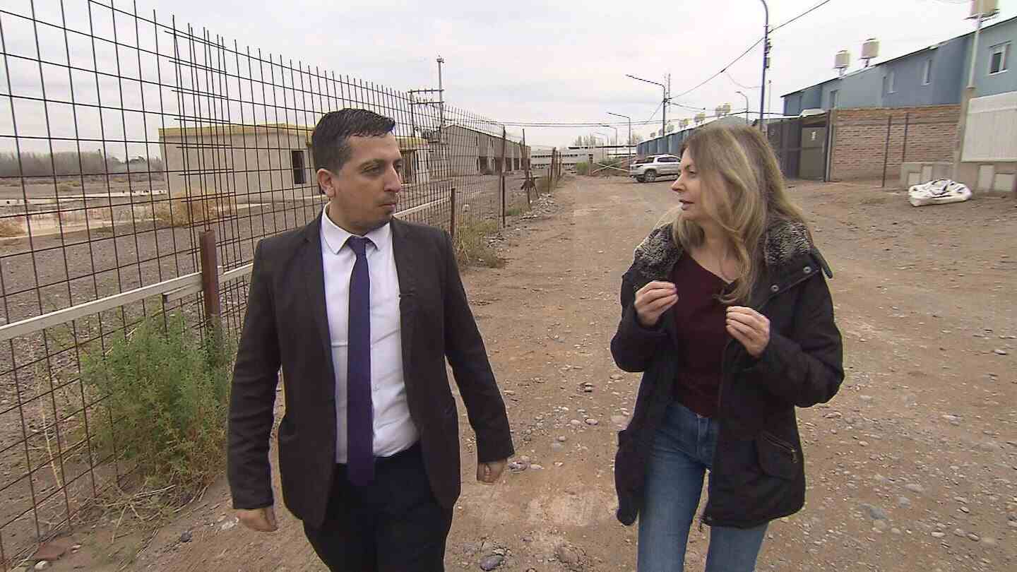 Jorge Salas caminando junto a una periodista en un terreno vacío en Neuquén