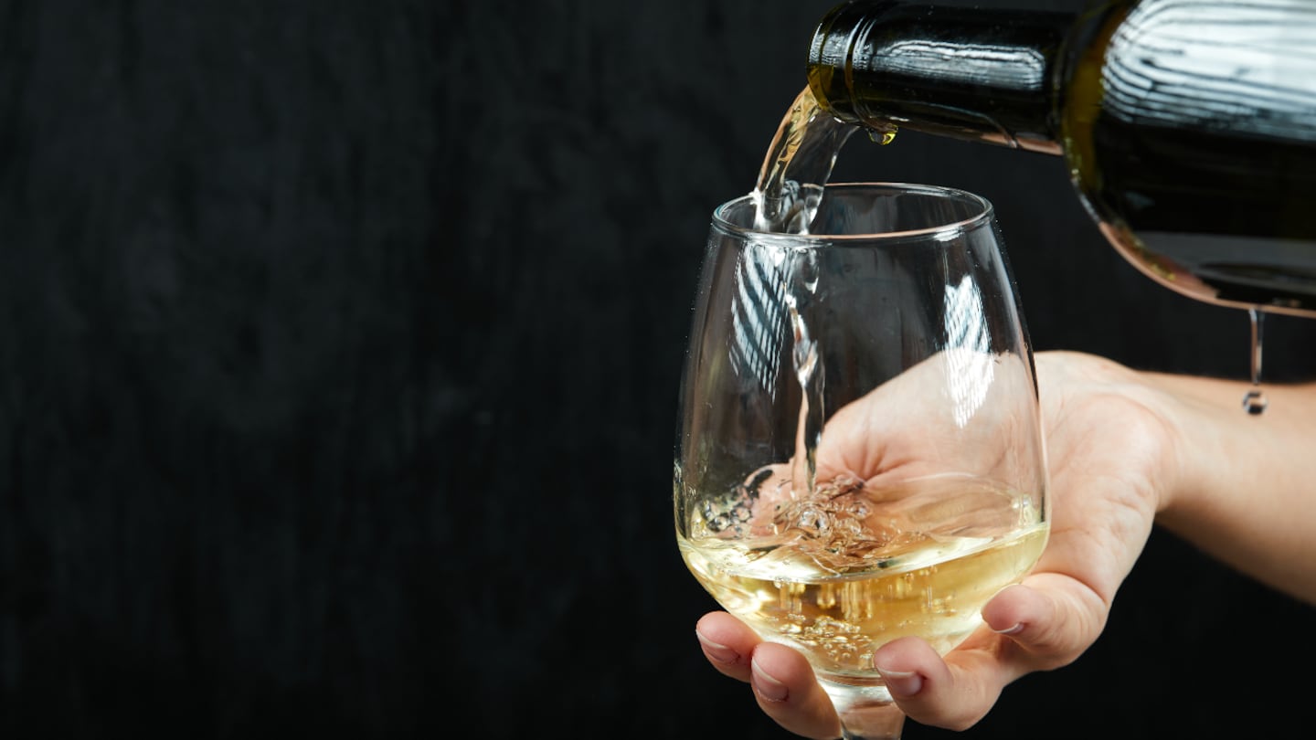 Vaso de vino blanco siendo servido por una mano