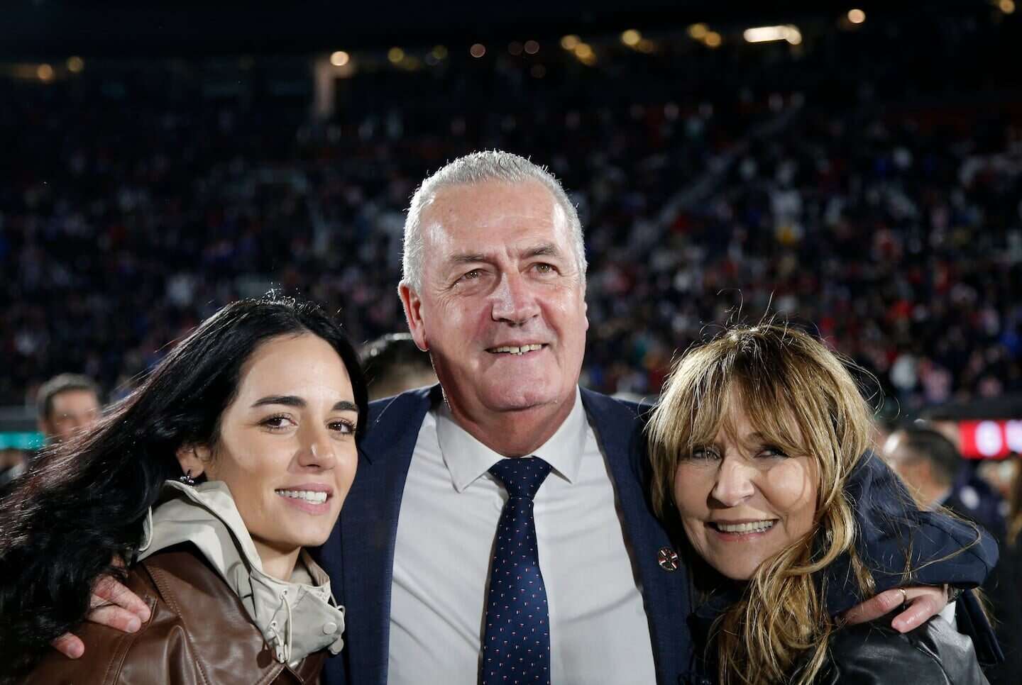 Gustavo Alfaro posando con dos mujeres sonrientes en un evento deportivo