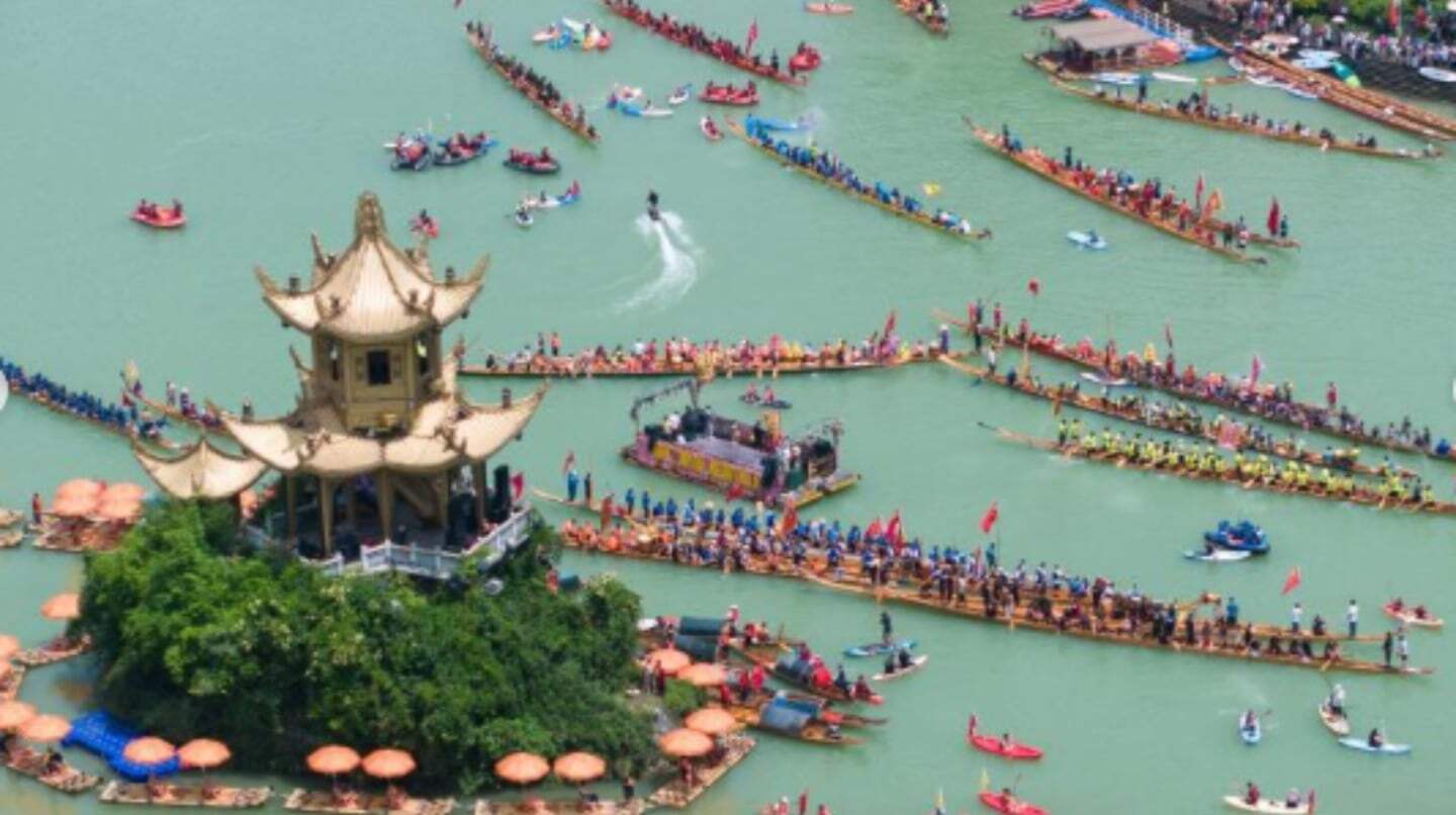 Vista aérea del Festival del Bote del Dragón en Sichuan con botes en el agua y un templo en la isla