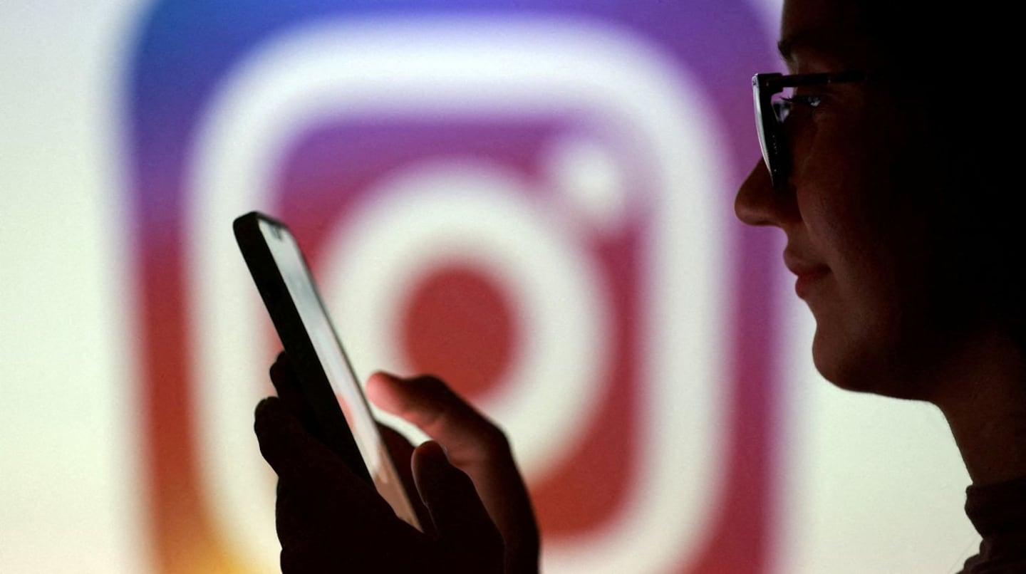 Persona usando un teléfono móvil frente al logo de Instagram