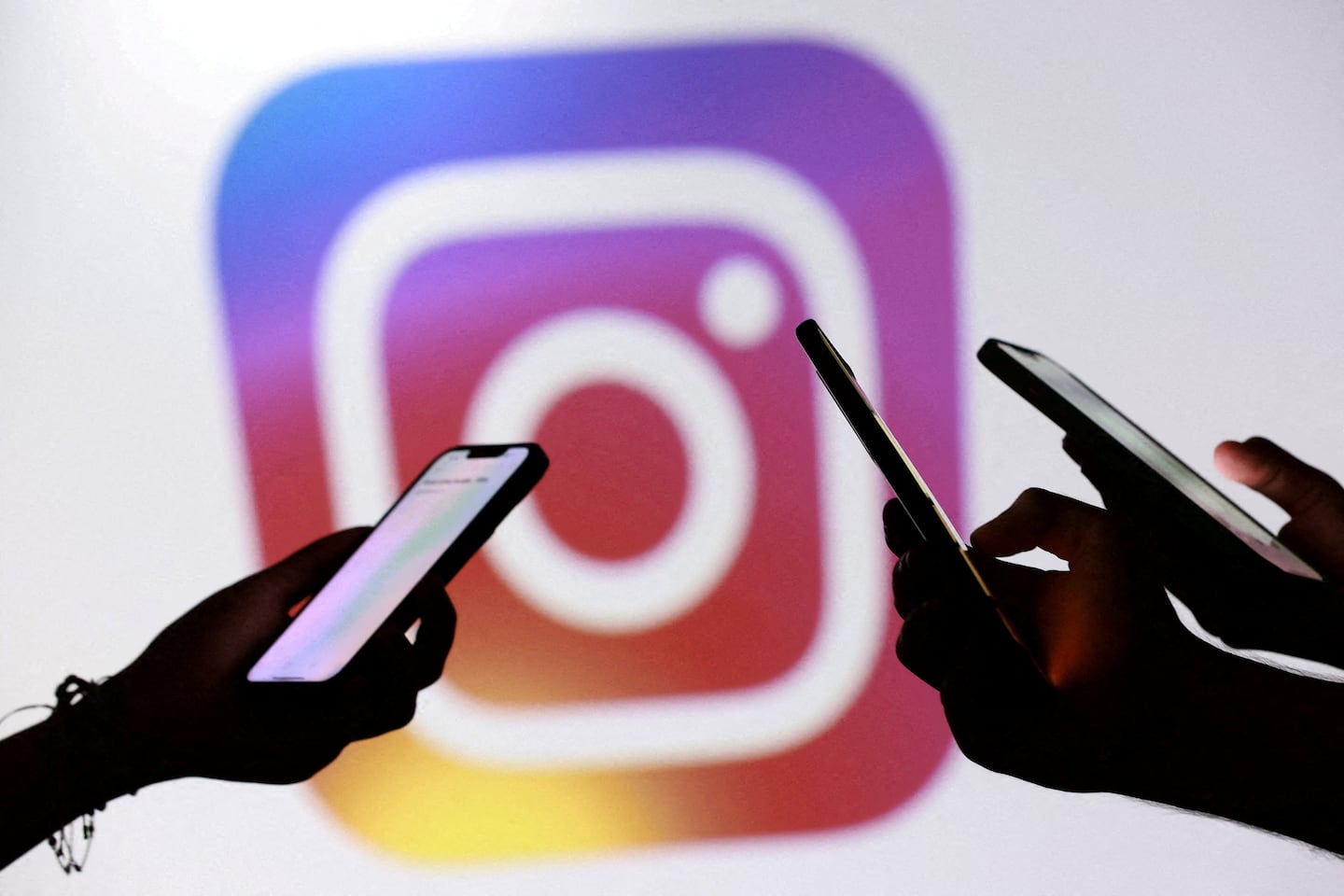 Siluetas de personas sosteniendo teléfonos móviles frente al logo de Instagram