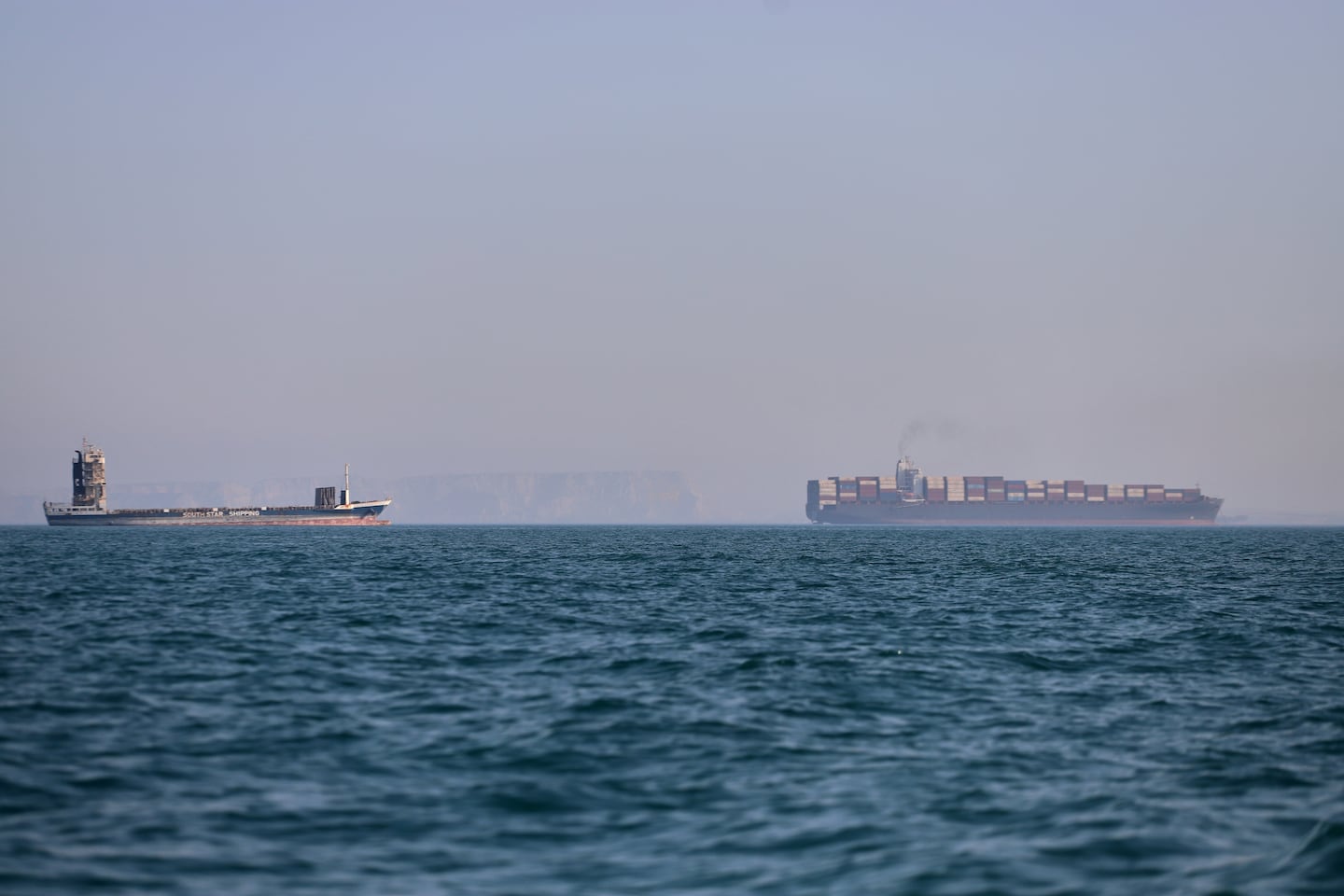 Dos barcos en el mar, uno de carga y otro de menor tamaño, en un ambiente de neblina