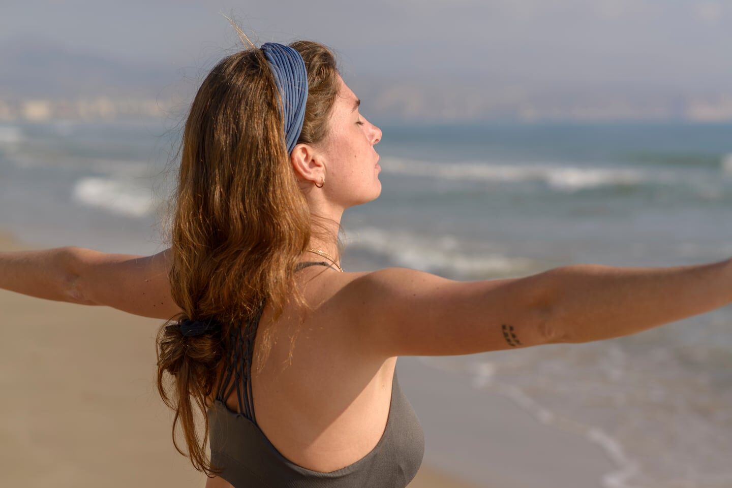 Mujer con los brazos abiertos frente al mar, simbolizando libertad y conexión con la naturaleza
