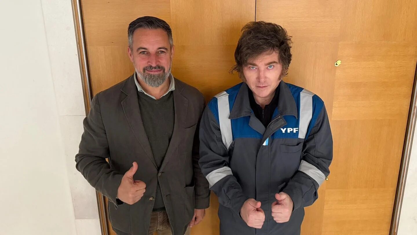 Javier Milei y un hombre posando con pulgares hacia arriba frente a una puerta