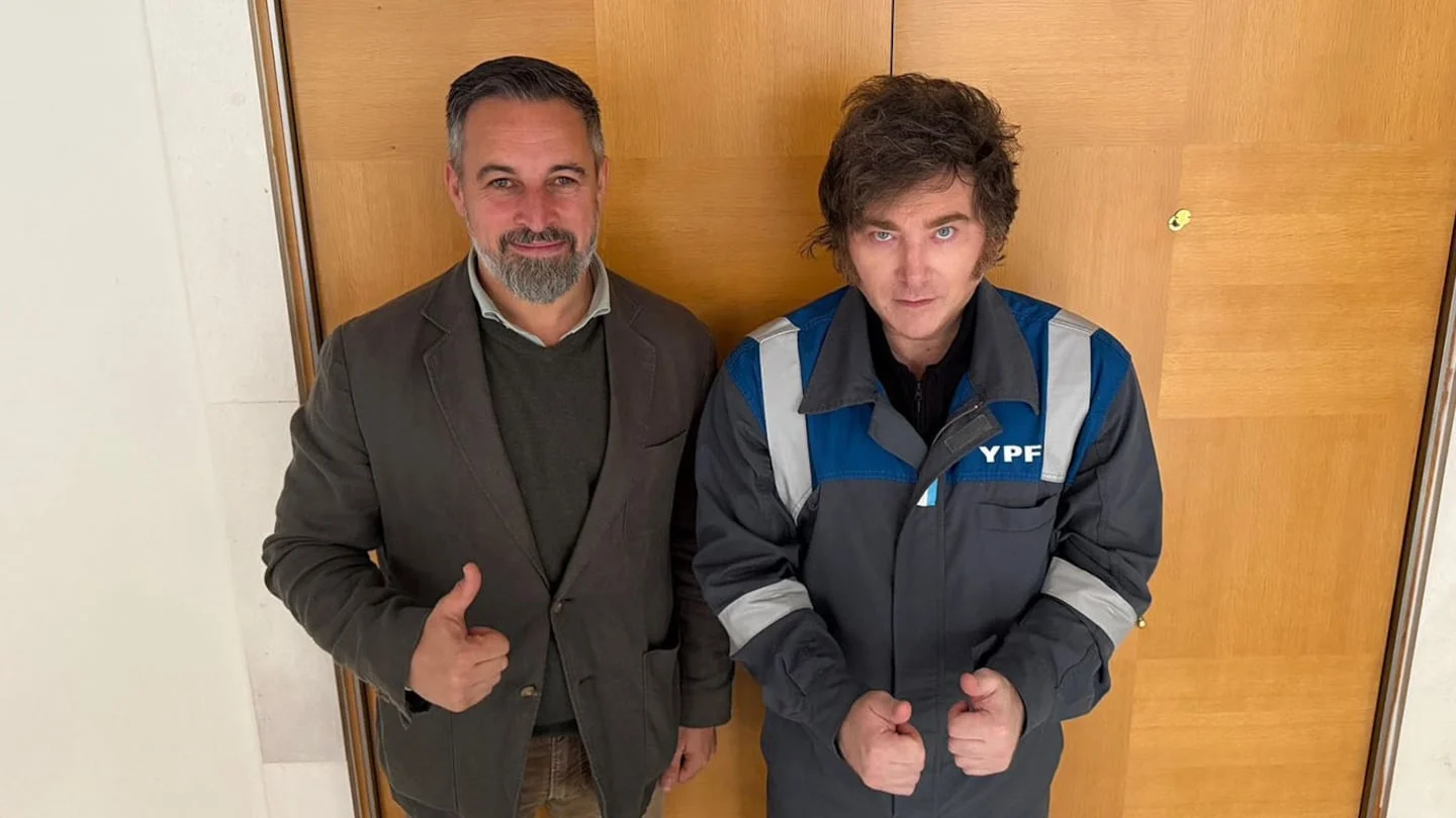 Javier Milei y un hombre posando con pulgares hacia arriba frente a una puerta