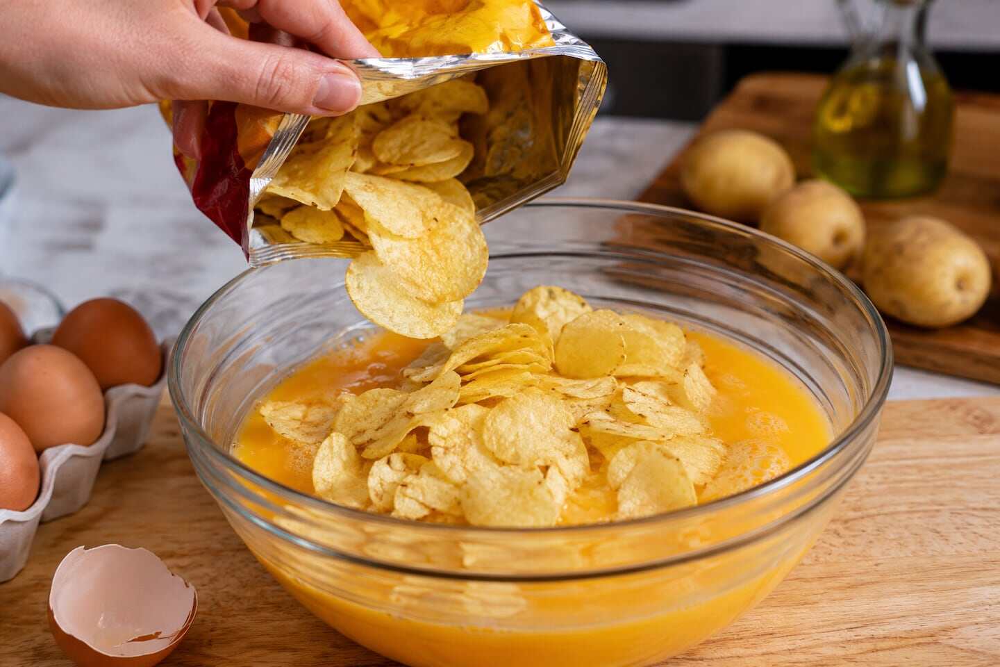 Mano vertiendo papas fritas en un bol con huevos batidos para hacer tortilla de papas