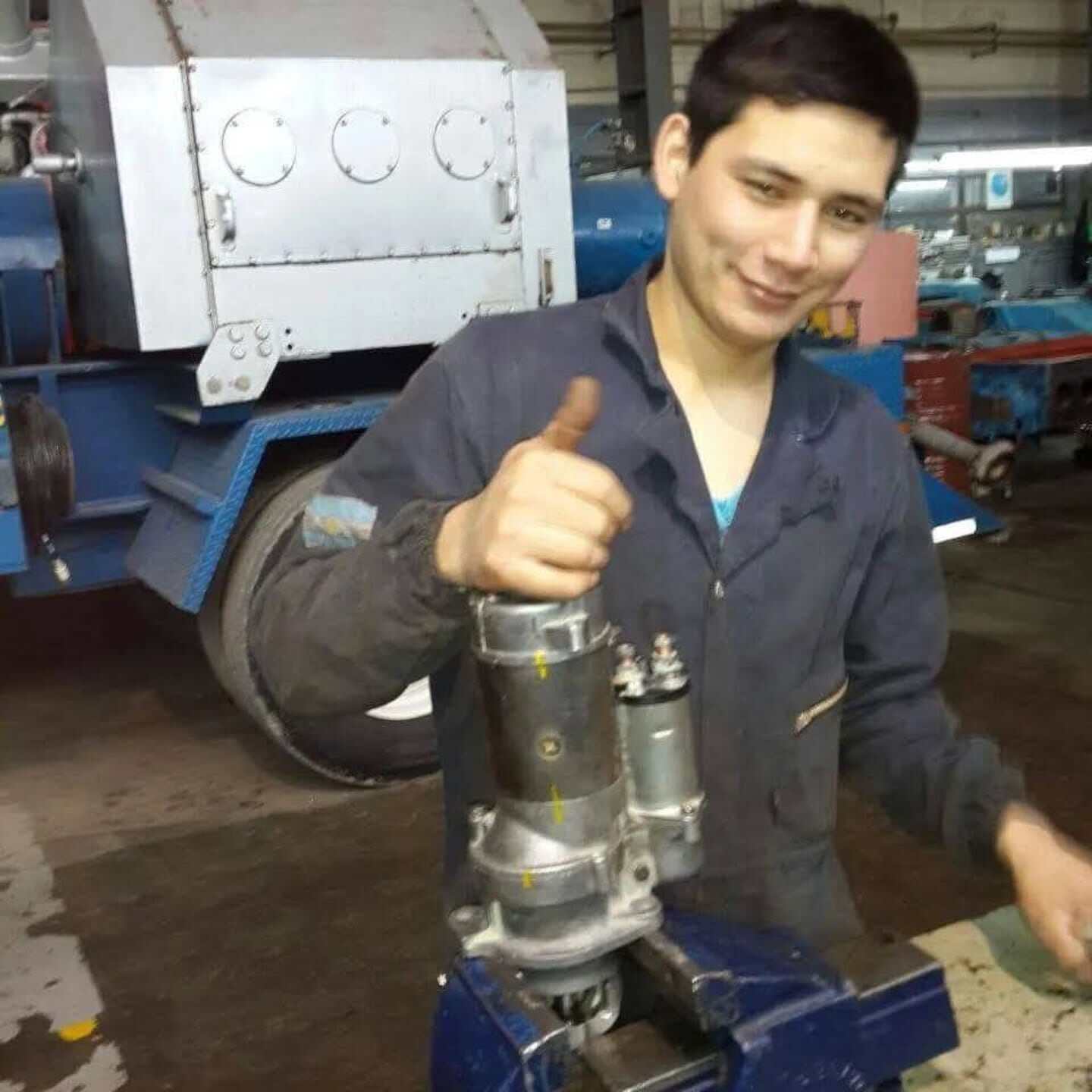 Julio Inostroza, mecánico en su taller, sonríe mientras trabaja en una pieza de maquinaria