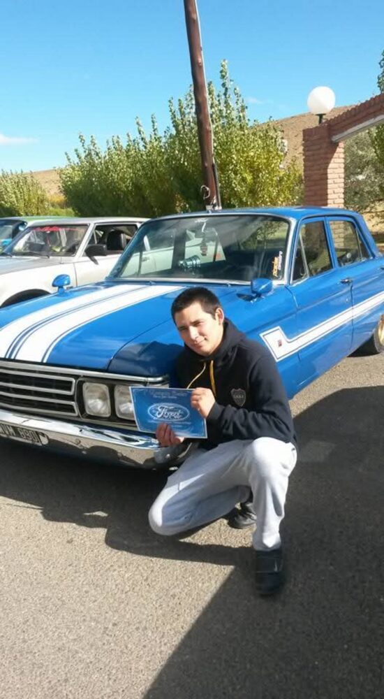 Julio Inostroza posando junto a un automóvil azul en su taller
