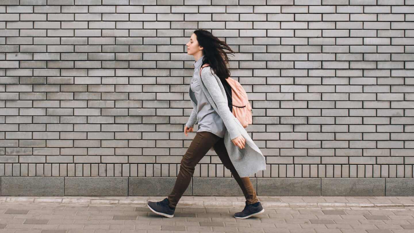 Mujer caminando frente a una pared de ladrillos grises