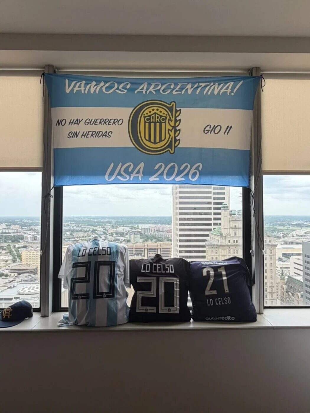 Tres camisetas de Lo Celso colgadas en una ventana con un cartel de apoyo para el Mundial 2026