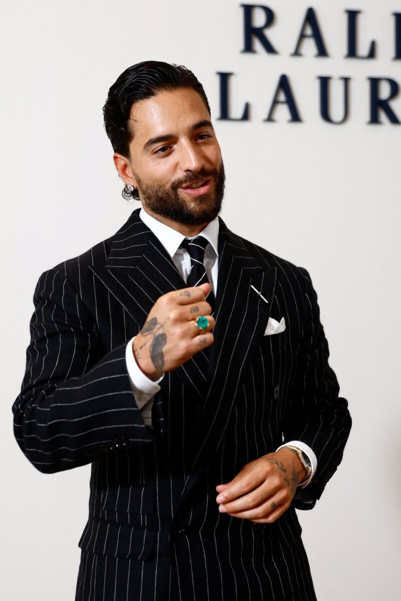 Maluma sonriendo mientras viste un traje a rayas en un evento