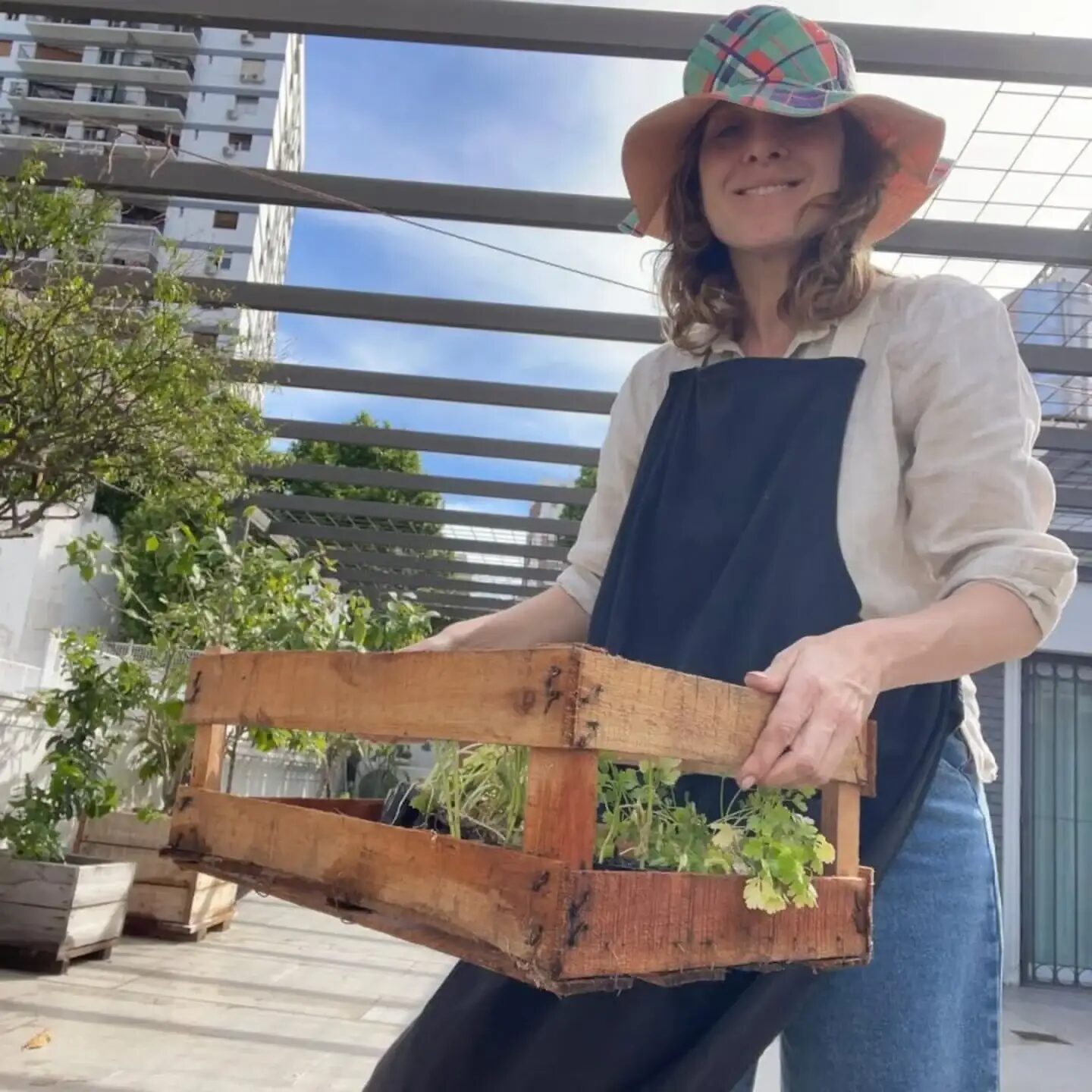 Carla Peterson sosteniendo una caja de madera con plantas en su huerta urbana
