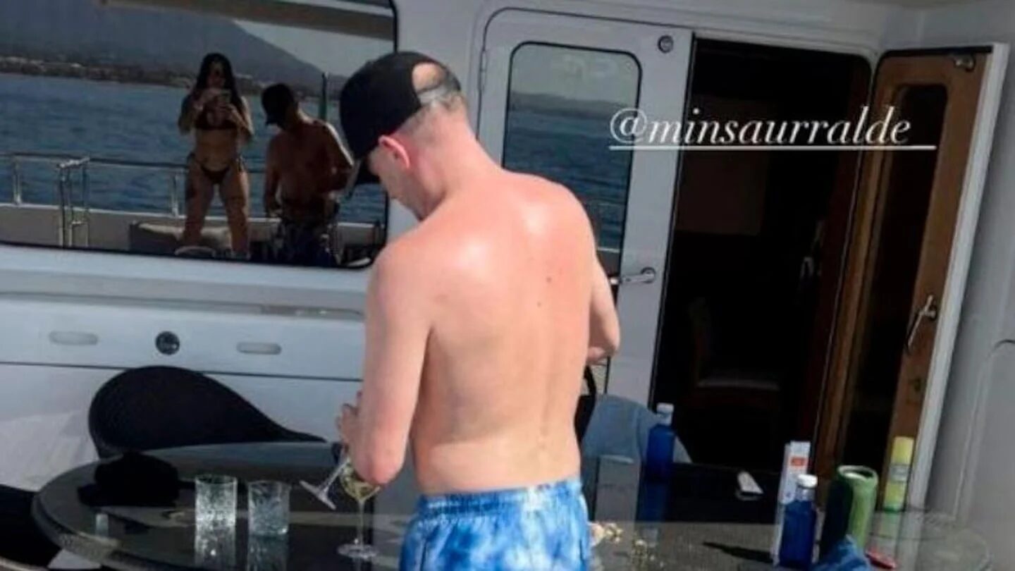 Martín Insaurralde en un yate, de espaldas, mientras sostiene una copa en una mesa