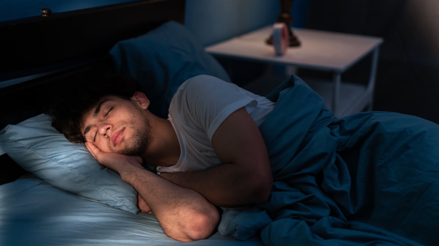 Joven durmiendo en una cama con sábanas azules