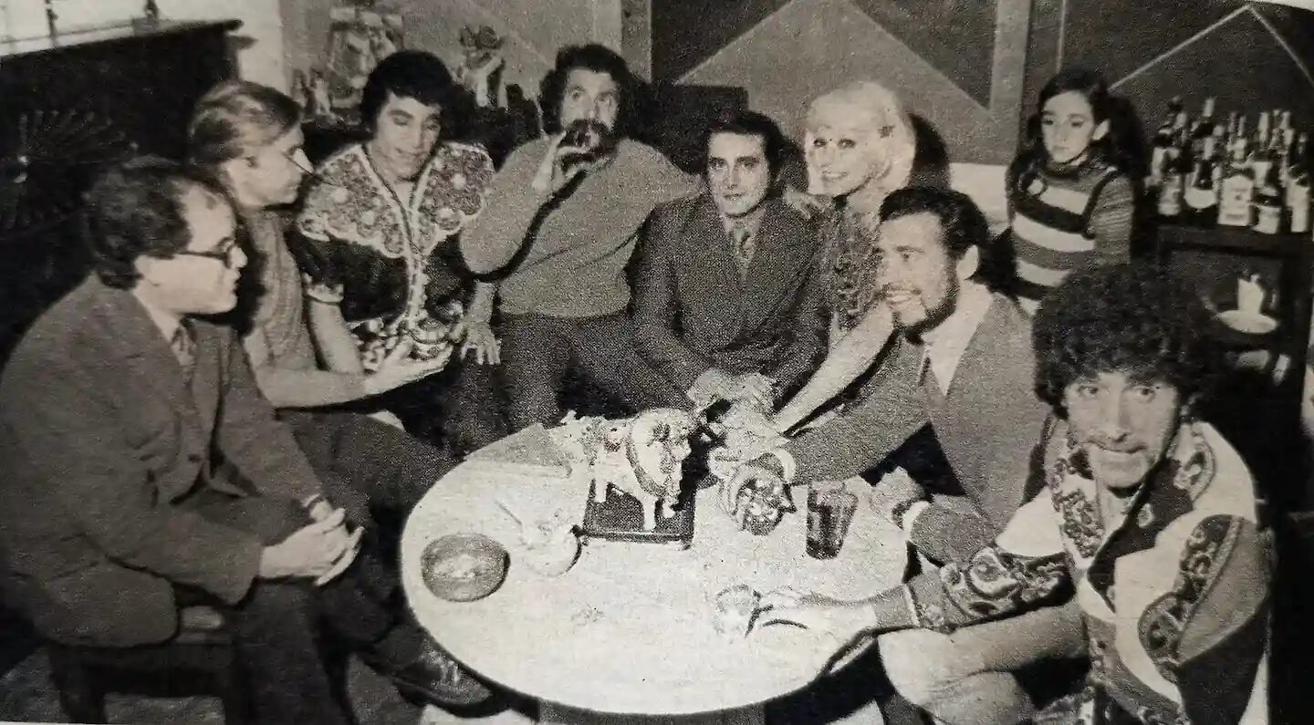 Grupo de personas reunidas alrededor de una mesa en un ambiente social, posiblemente durante un evento relacionado con el Prode