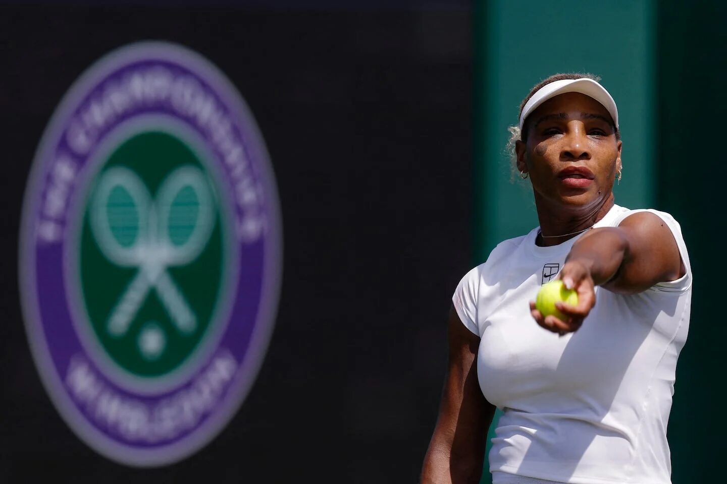 Tenista lanzando una pelota en Wimbledon con el logo del torneo de fondo