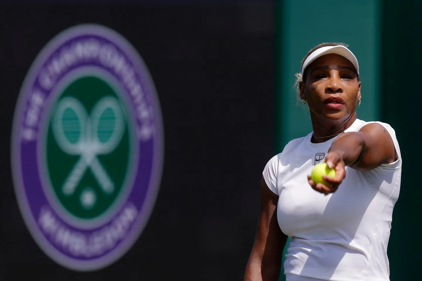 Tenista lanzando una pelota en Wimbledon con el logo del torneo de fondo