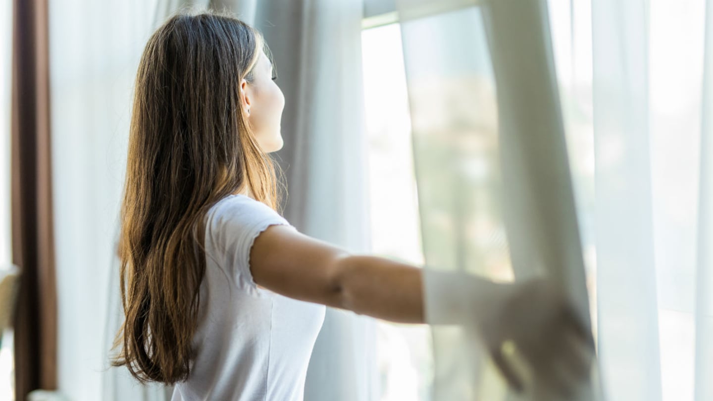 Mujer disfrutando de la luz matutina al abrir las cortinas