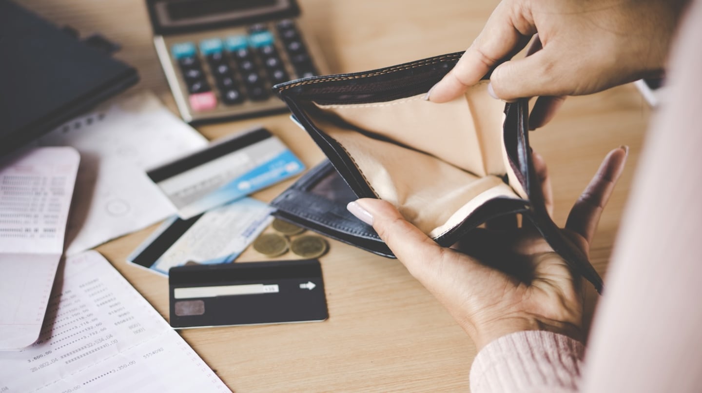 Persona revisando una billetera vacía junto a tarjetas de crédito y documentos financieros