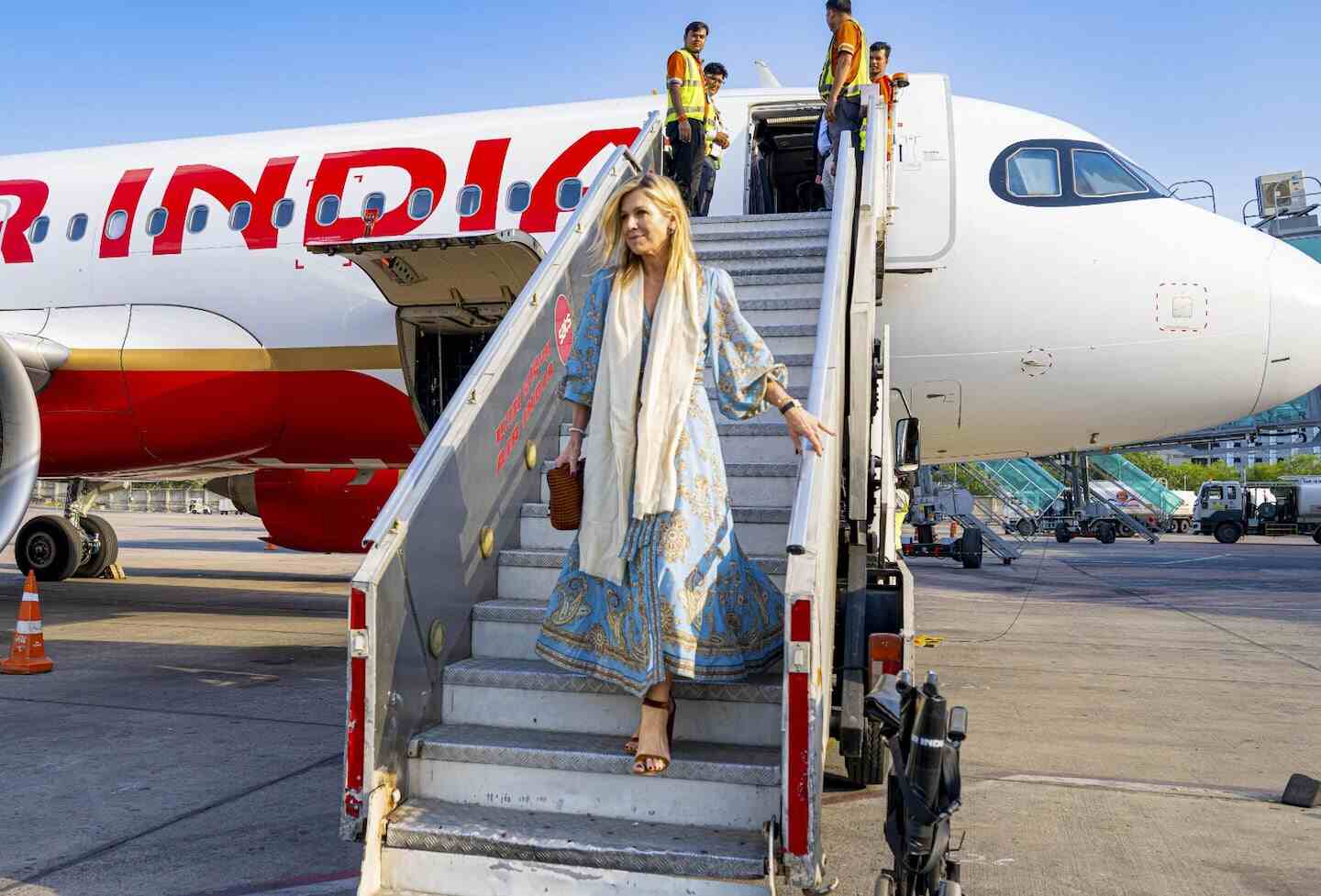 La reina Máxima de los Países Bajos descendiendo de un avión en India con un vestido celeste y un bolso argentino