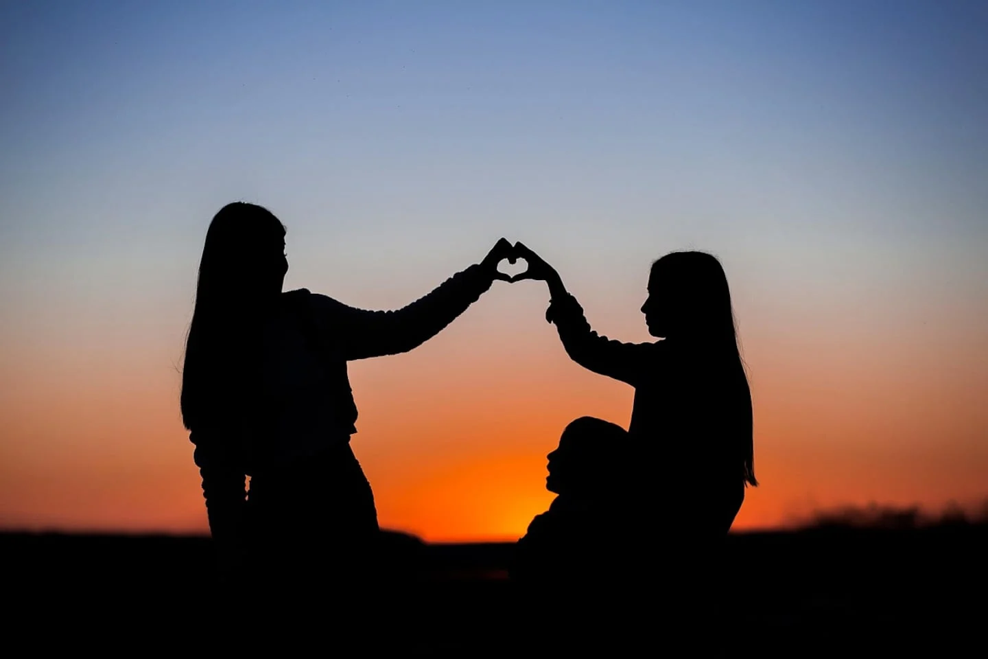 Silhouette de tres personas formando un corazón con las manos al atardecer