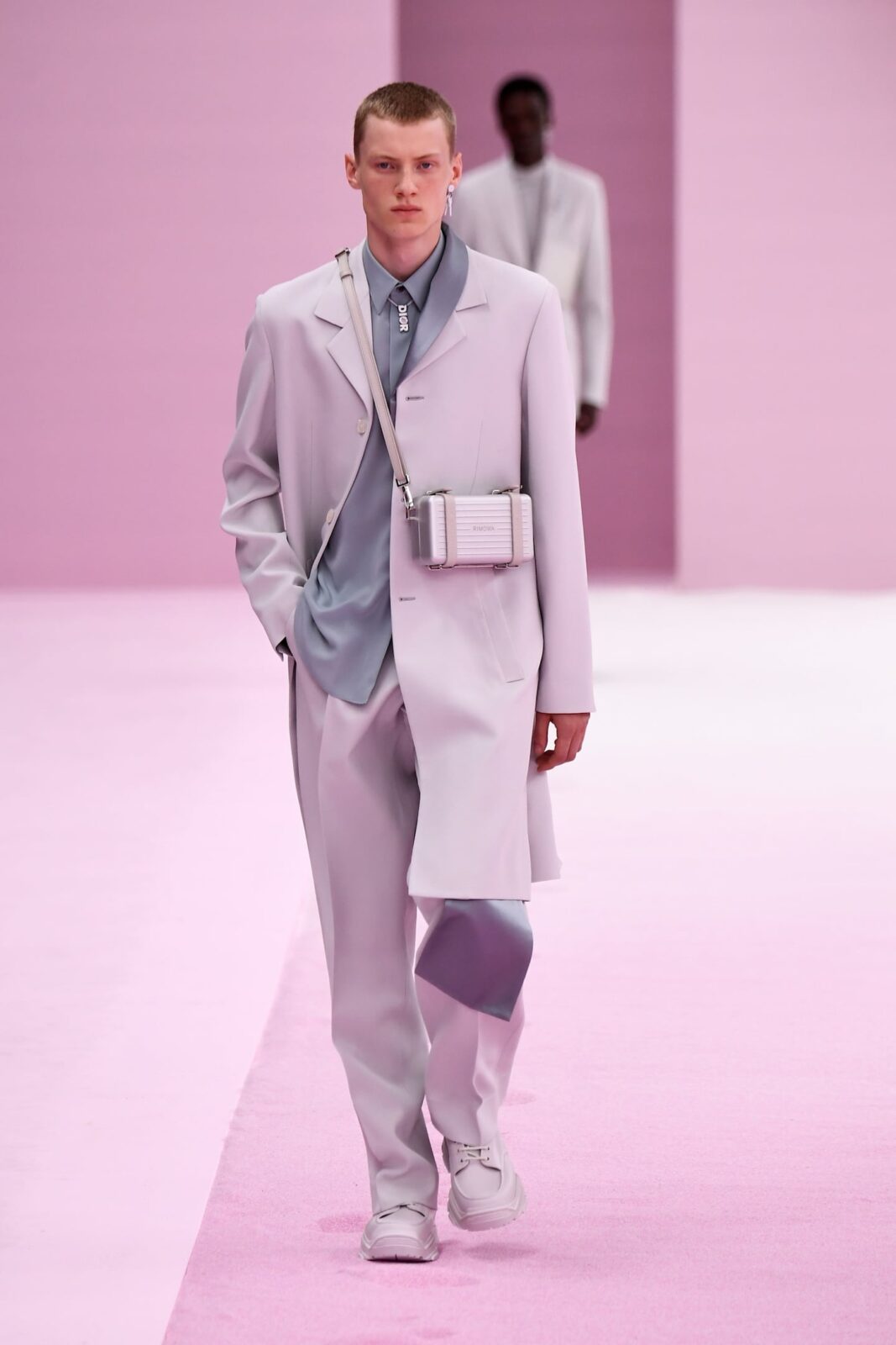 Modelo masculino desfilando en la Semana de la Moda Masculina de París con un traje claro y accesorios modernos