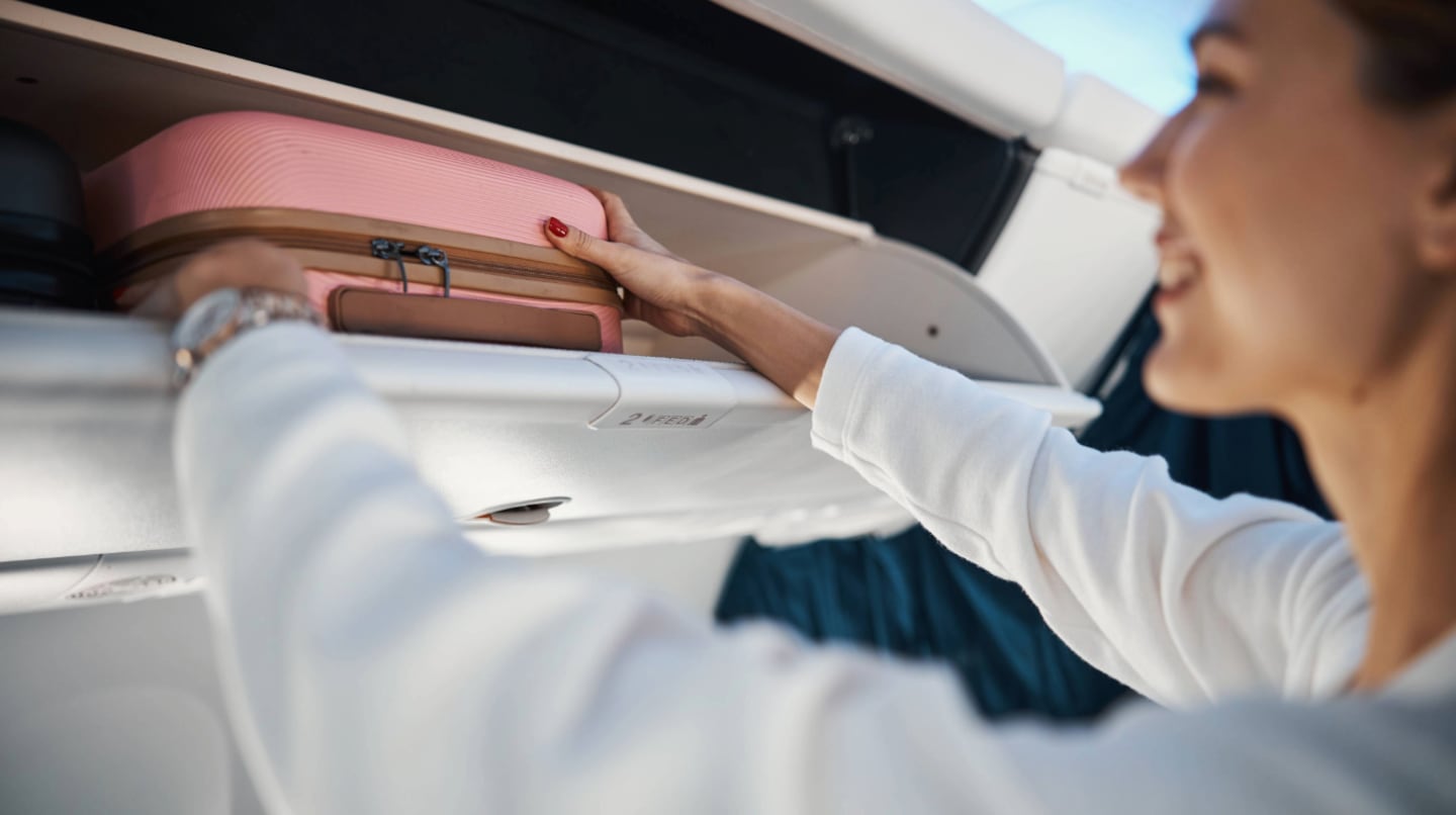 Mujer colocando una maleta de mano en el compartimento superior de un avión