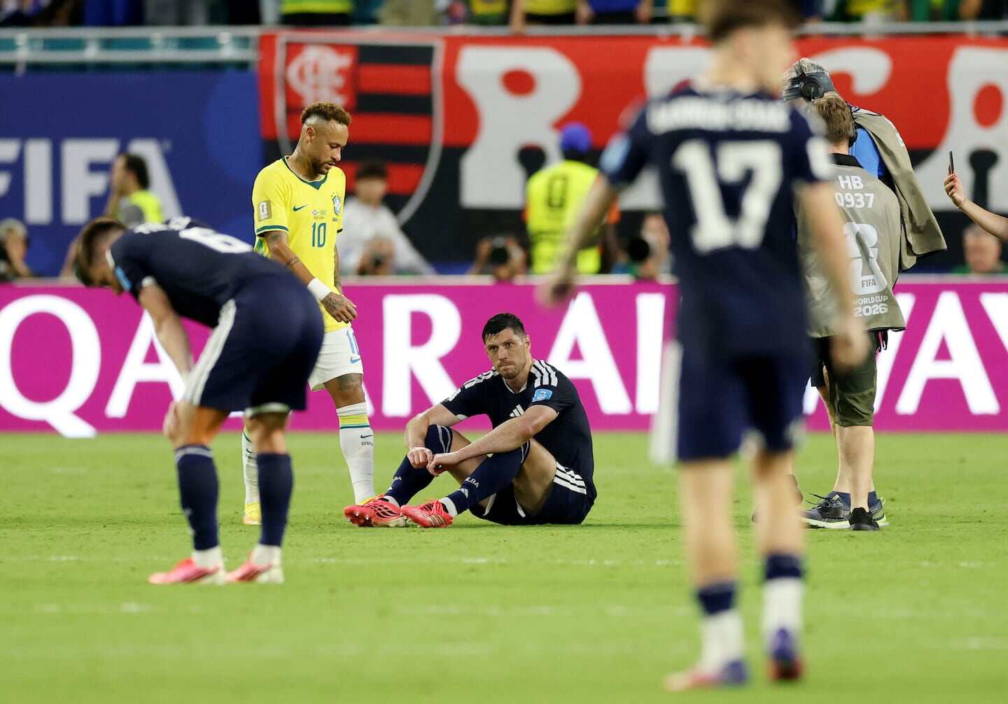 Jugadores de Brasil y Escocia en un partido del Mundial, con un jugador escocés sentado en el suelo