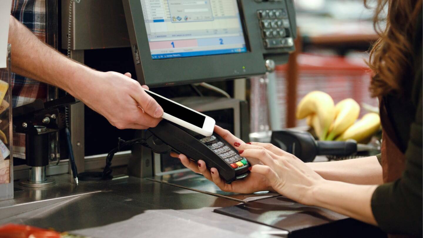 Cliente realizando un pago con teléfono móvil en una caja de supermercado