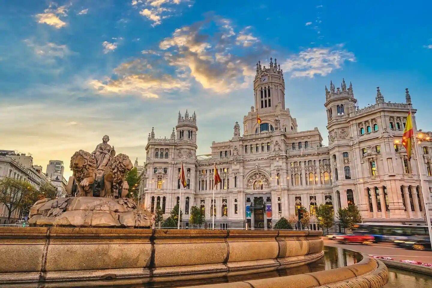 Edificio histórico con fuente y estatuas en primer plano bajo un cielo azul con nubes