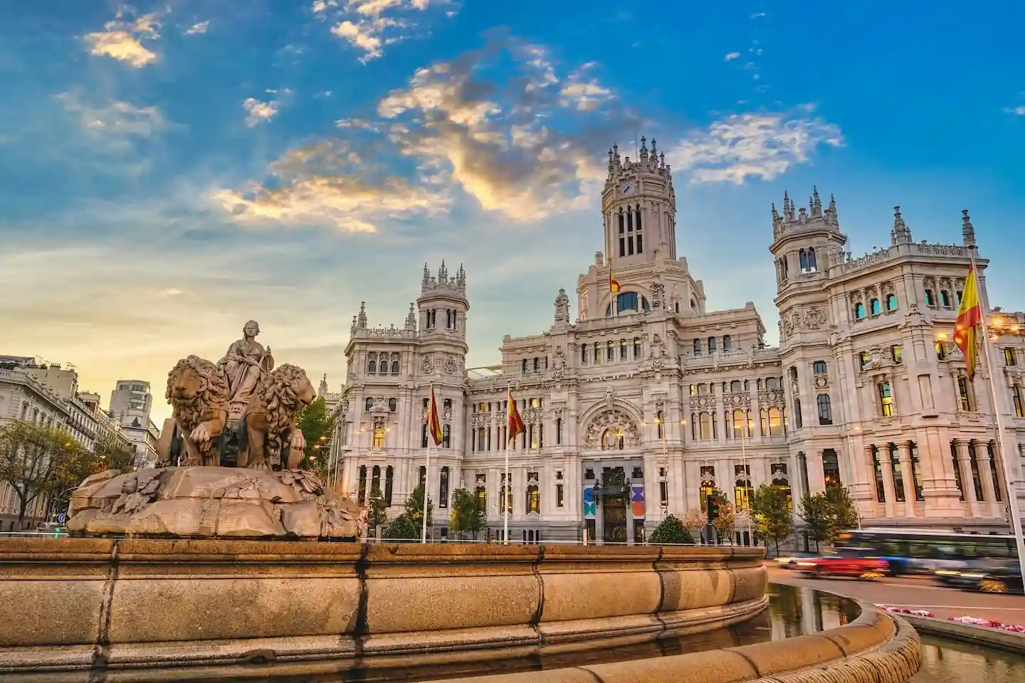 Edificio histórico con fuente y estatuas en primer plano bajo un cielo azul con nubes