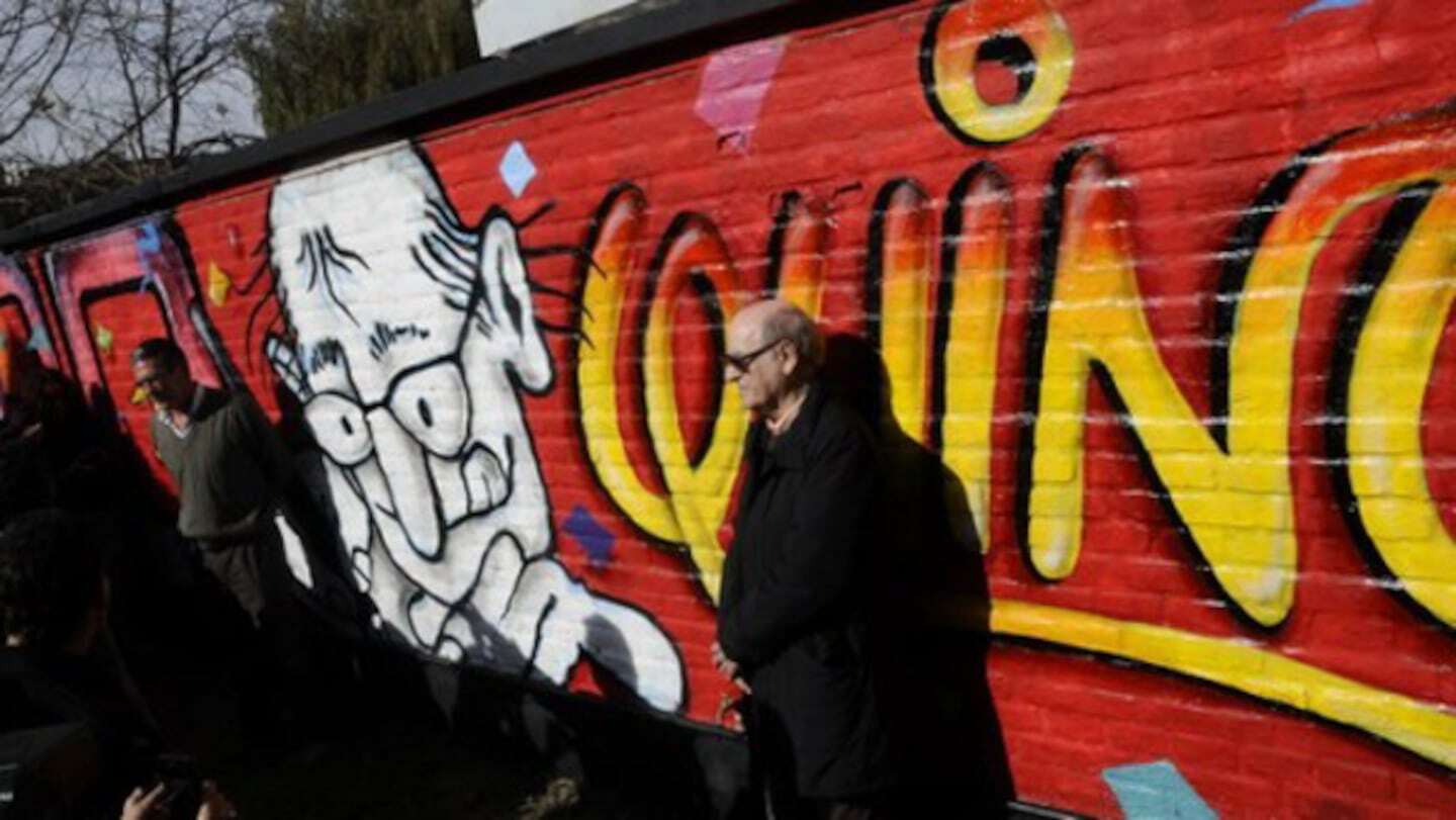 Hombre de pie junto a un mural de Quino en celebración del legado de Mafalda