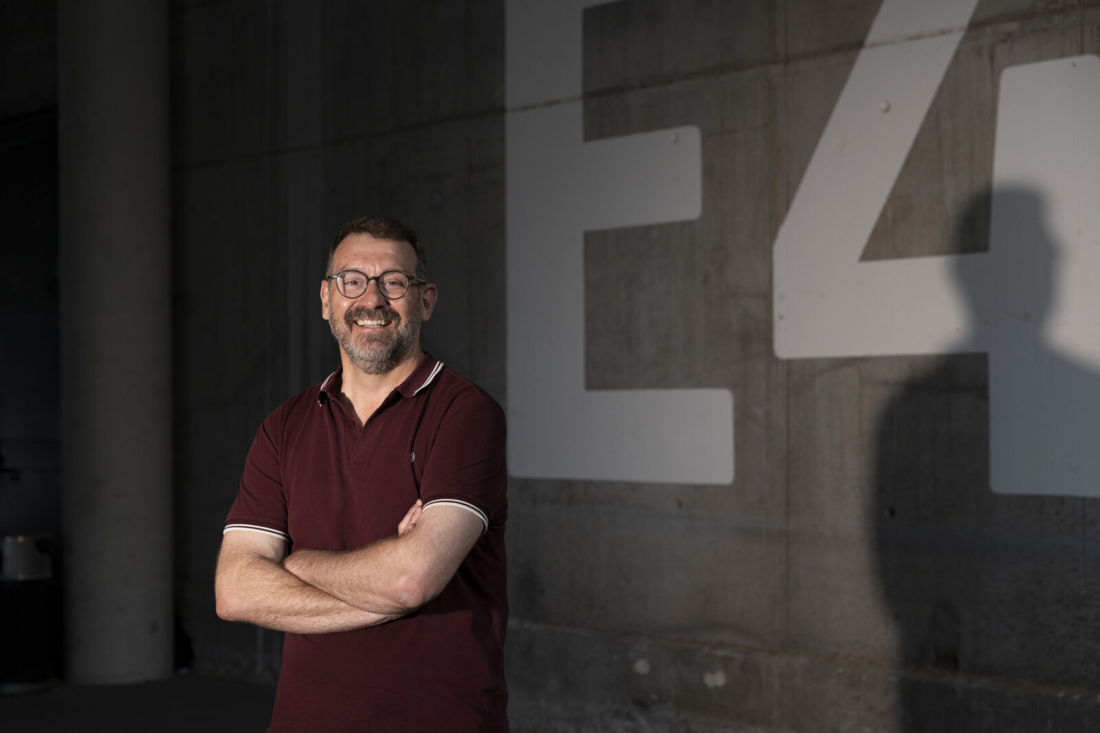 Marc Sala posando con una sonrisa en un entorno urbano con un fondo de concreto