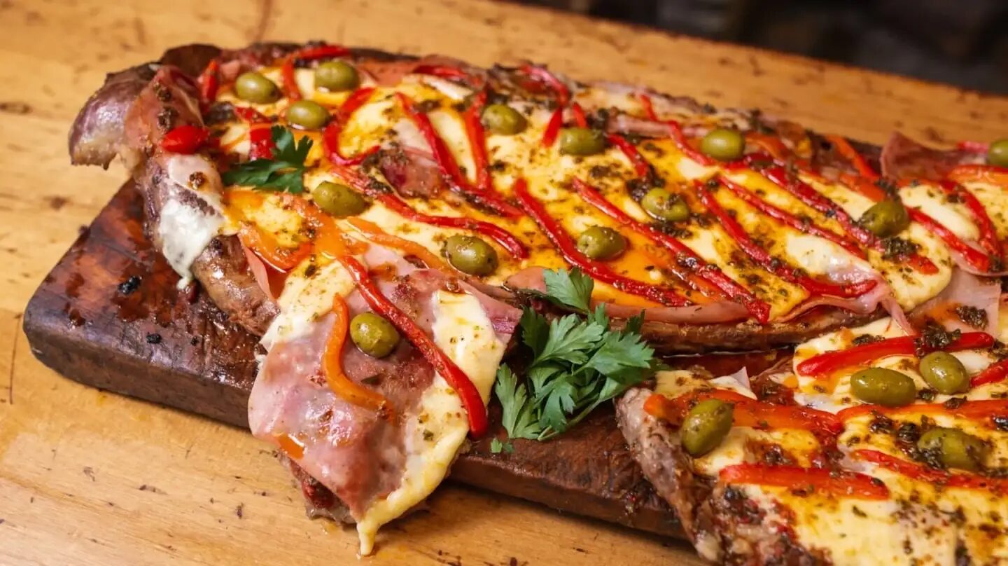Plato de carne asada con queso, pimientos y aceitunas sobre una tabla de madera