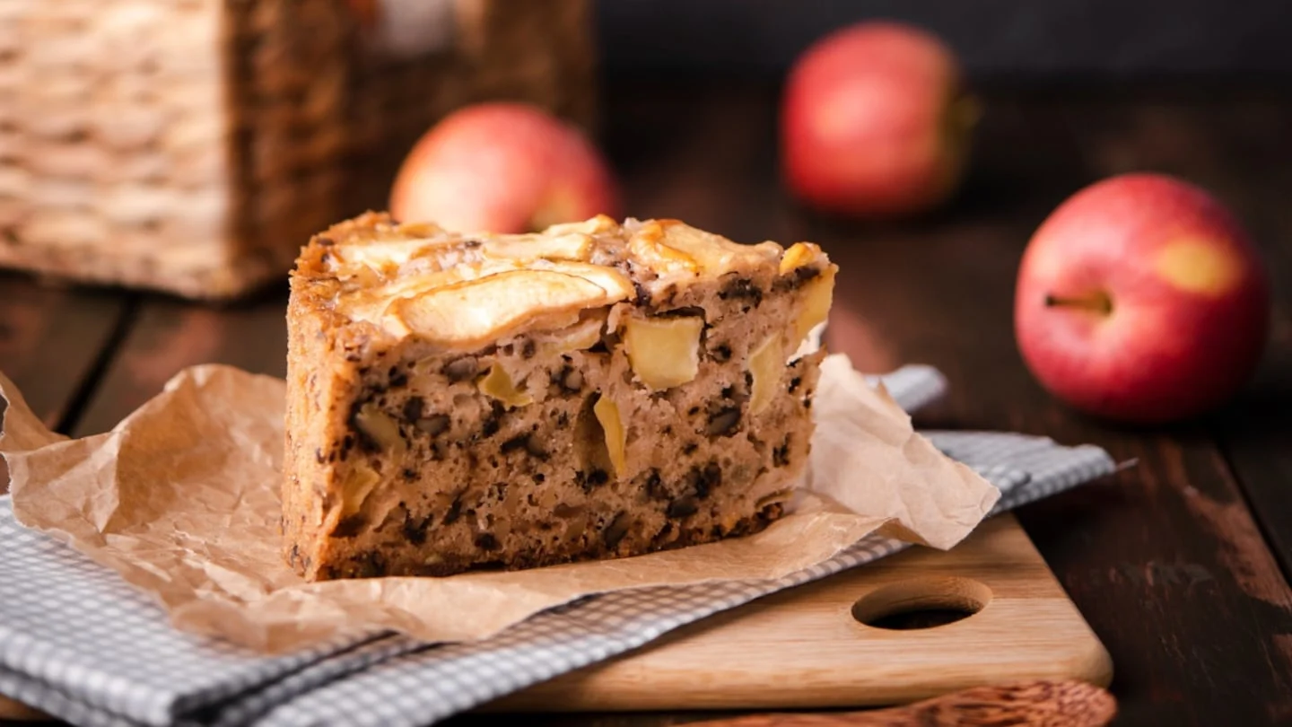 Tarta de manzana casera sobre una tabla de madera con manzanas al fondo