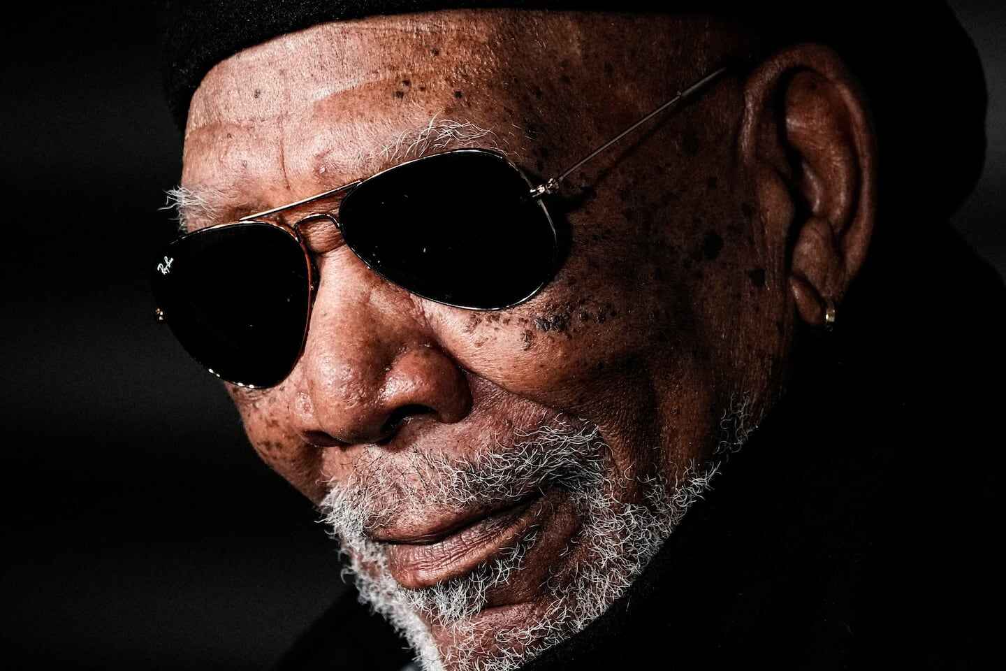 Morgan Freeman con gafas de sol y barba canosa, sonriendo levemente