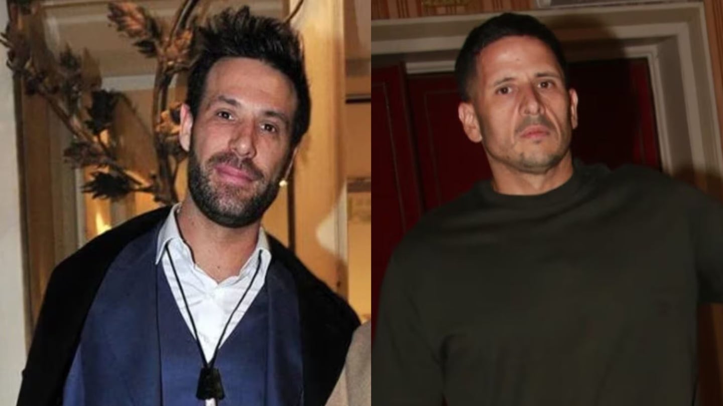 Dos hombres posando en un evento social, uno con chaqueta y el otro con un suéter oscuro