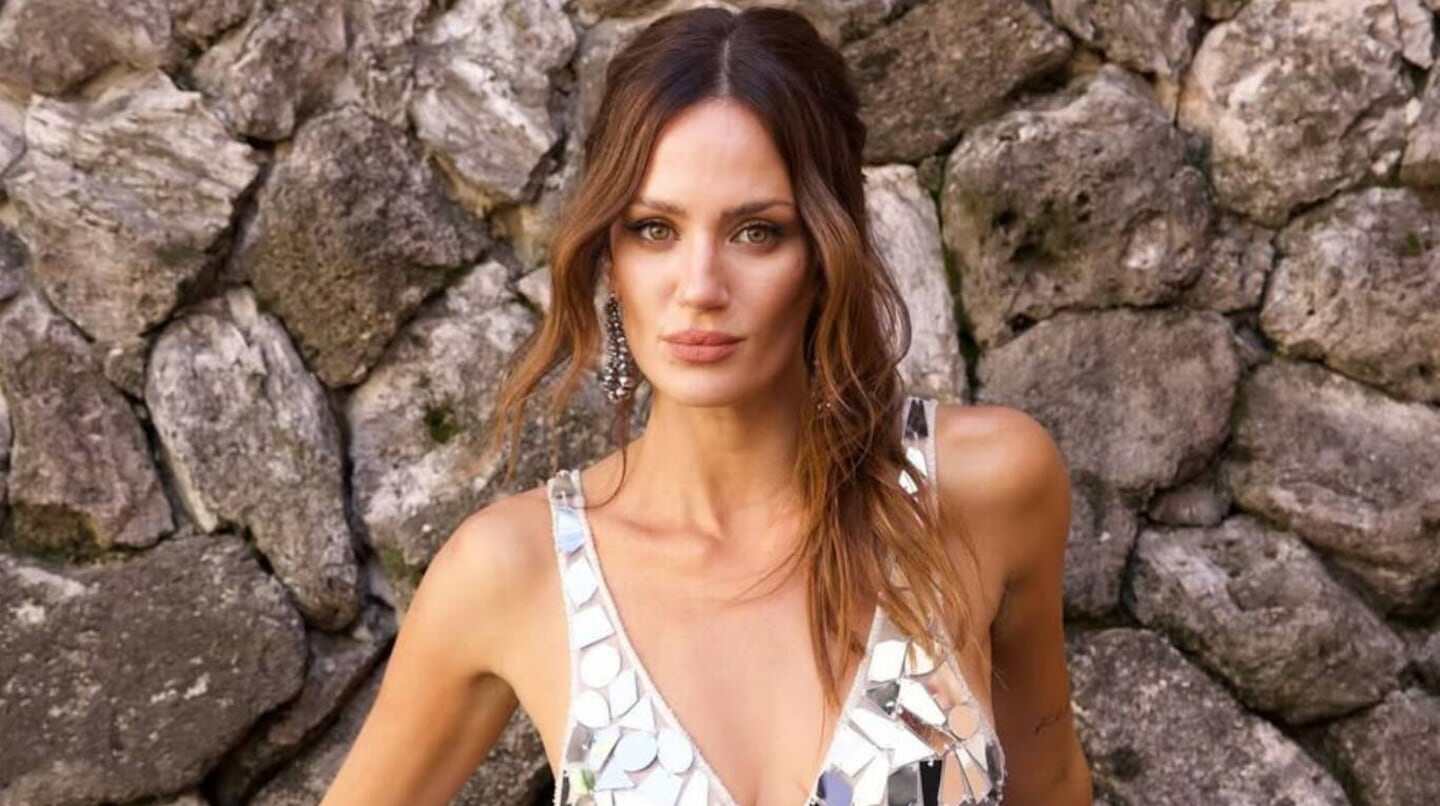 Paula Chaves posando con un vestido brillante frente a una pared de piedras