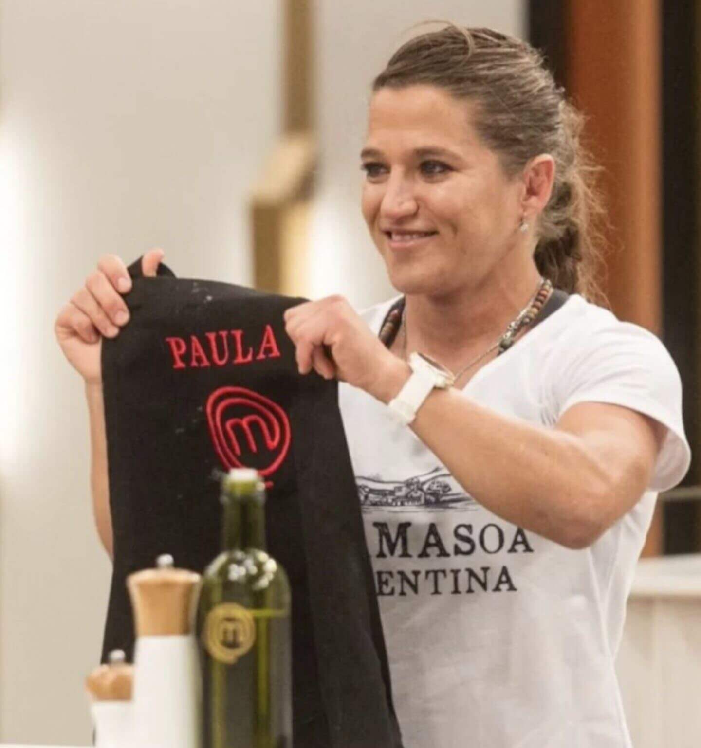 Paula Pareto sosteniendo una chaqueta de cocina con su nombre mientras sonríe