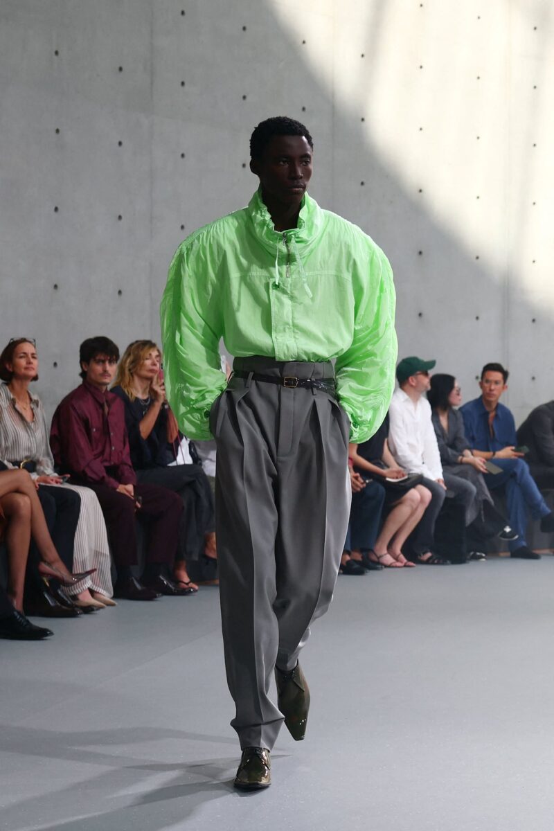 Modelo desfilando con una camisa verde brillante y pantalones grises en el evento de Pharrell Williams para Louis Vuitton en París