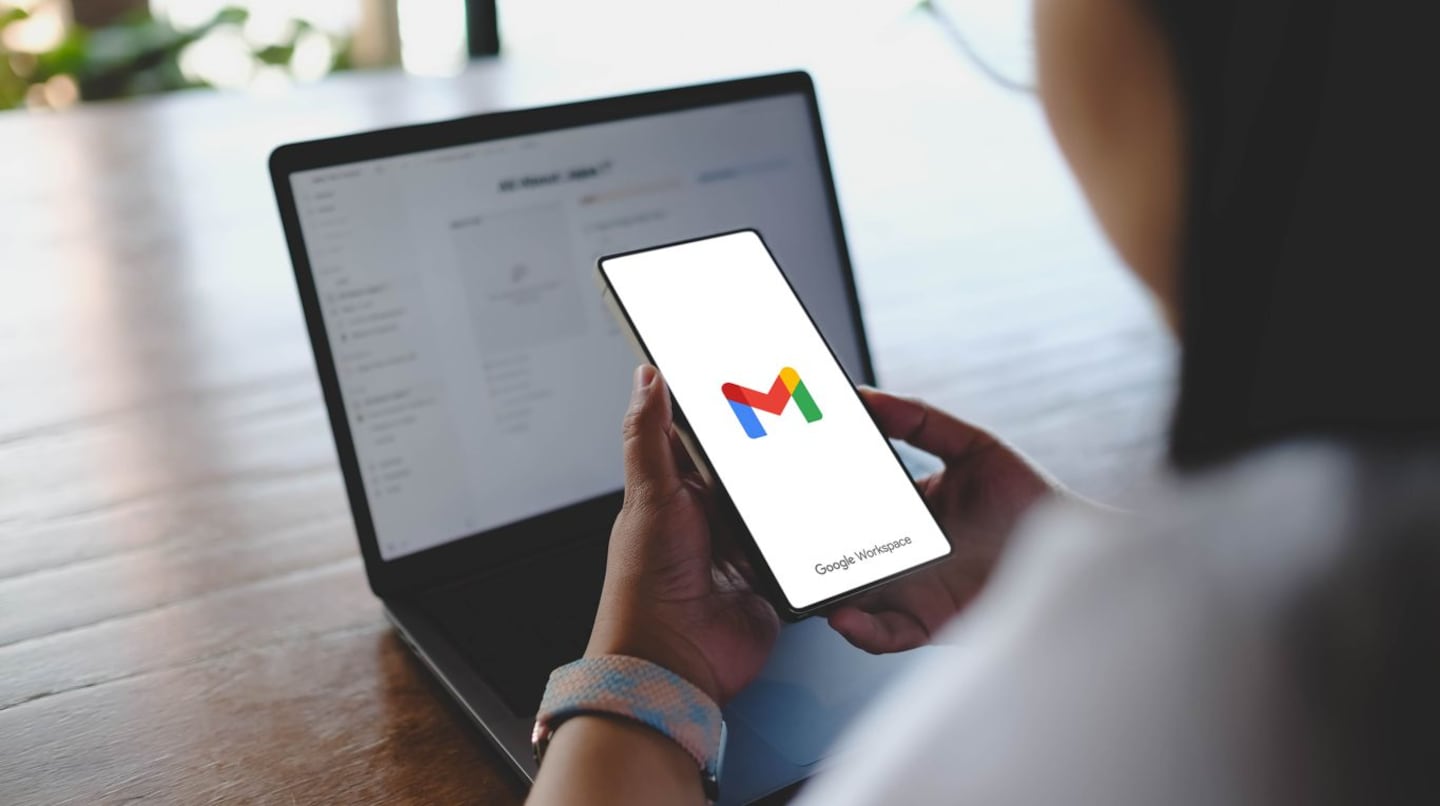 Usuario sosteniendo un teléfono con la aplicación de Gmail abierta frente a una laptop