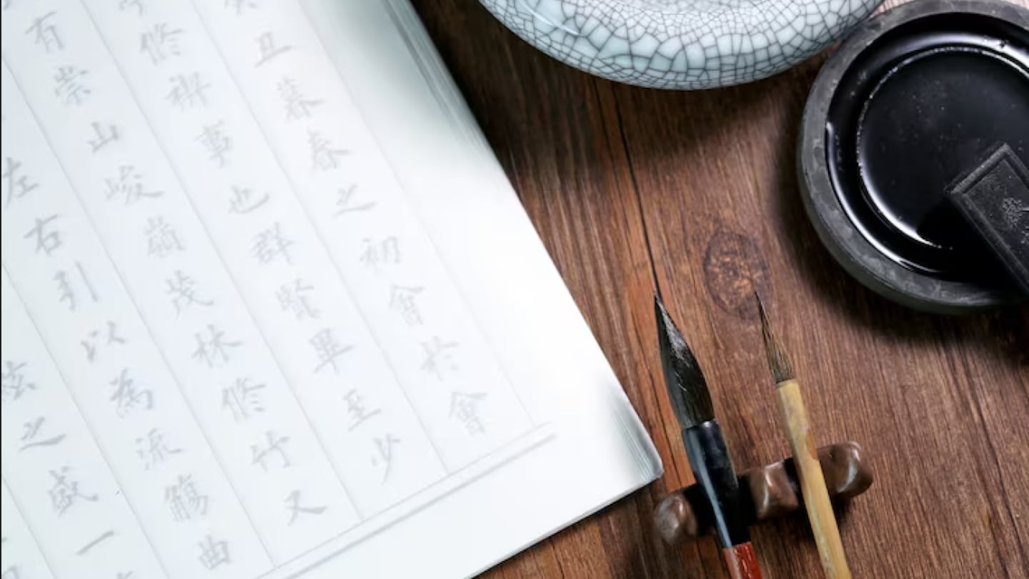 Papel con escritura china y herramientas de caligrafía sobre una mesa de madera