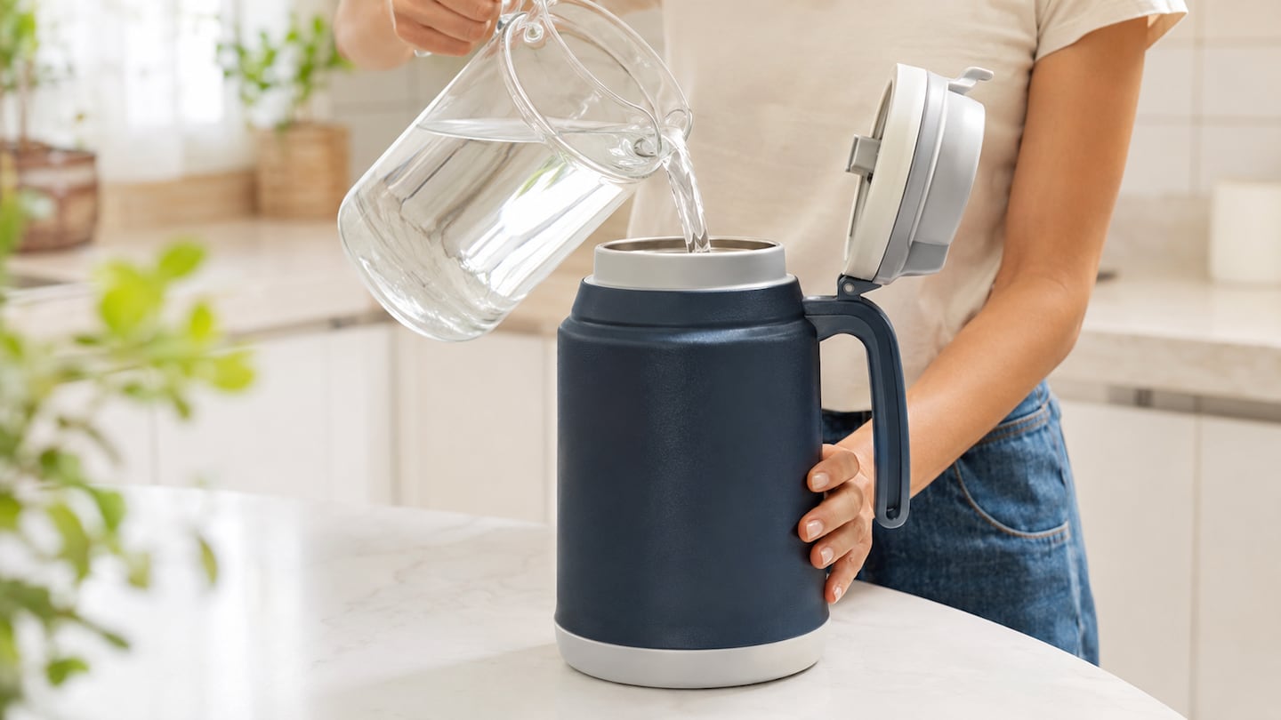 Persona vertiendo agua en un termo de acero inoxidable en una cocina moderna