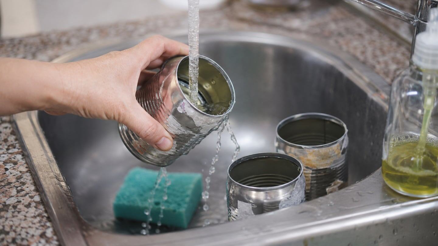 Mano vertiendo agua en latas recicladas en un fregadero