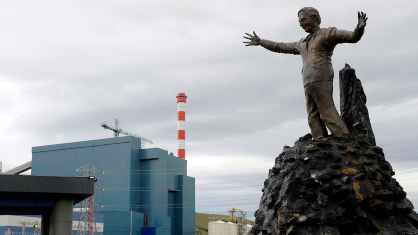 Estatua de un hombre con brazos extendidos frente a una planta industrial