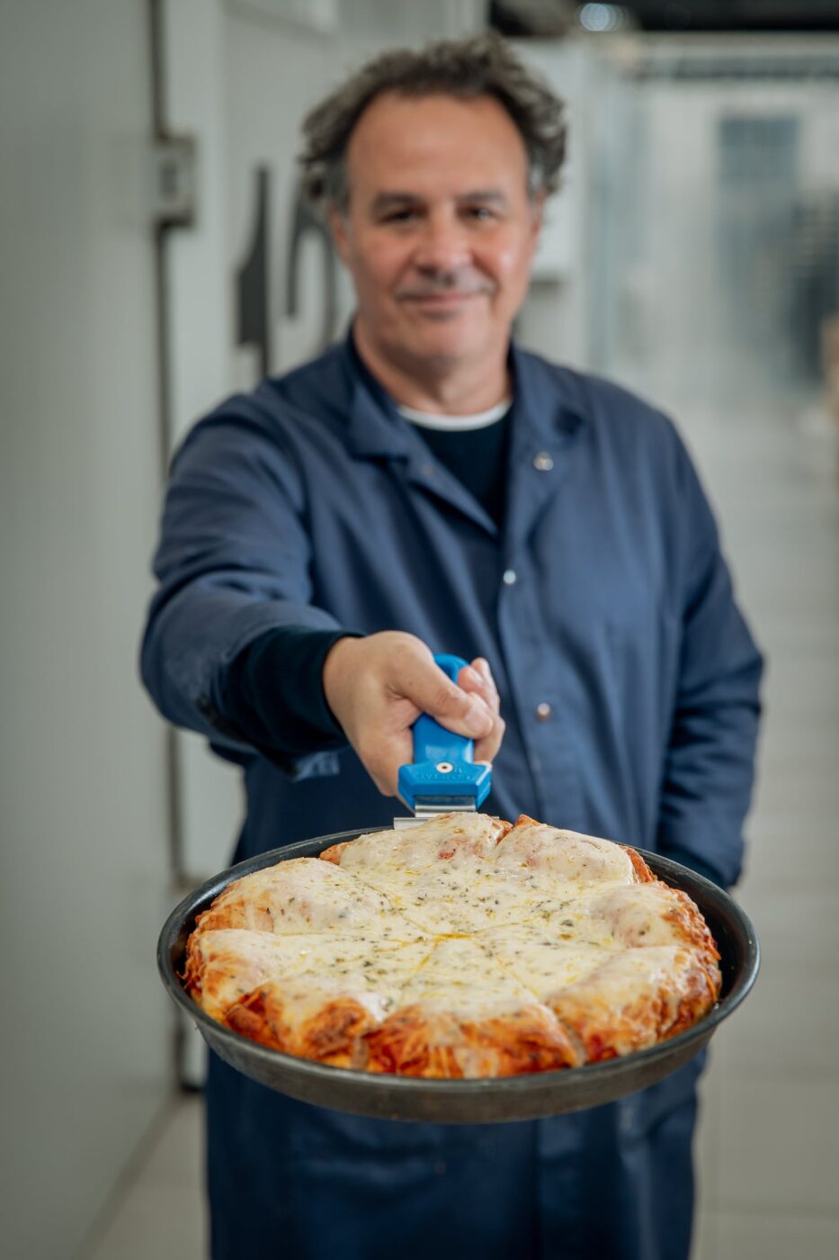 Chef Roberto Petersen sostiene una pizza al molde lista para hornear