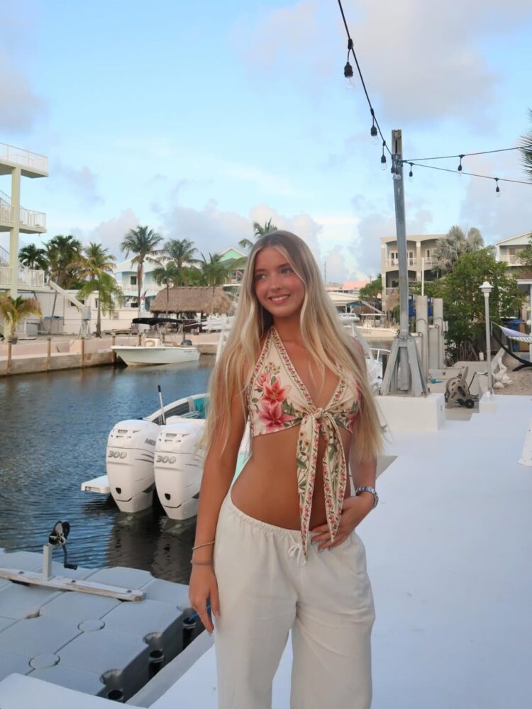 Aitana Paladini, hija de Rocío Guirao Díaz, sonríe en un entorno costero con un top floral y pantalones claros
