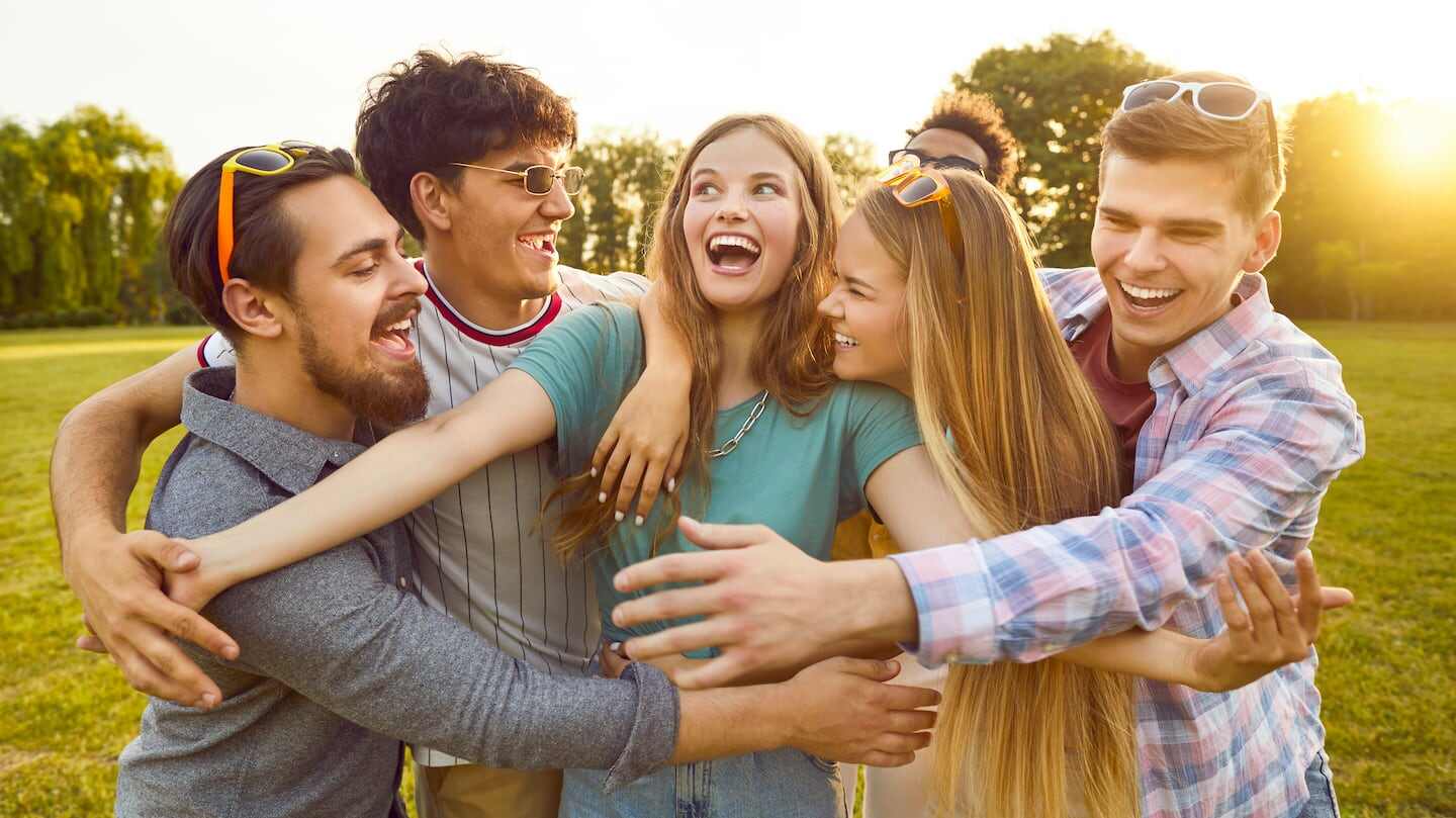 Grupo de amigos sonriendo y abrazándose en un parque al atardecer
