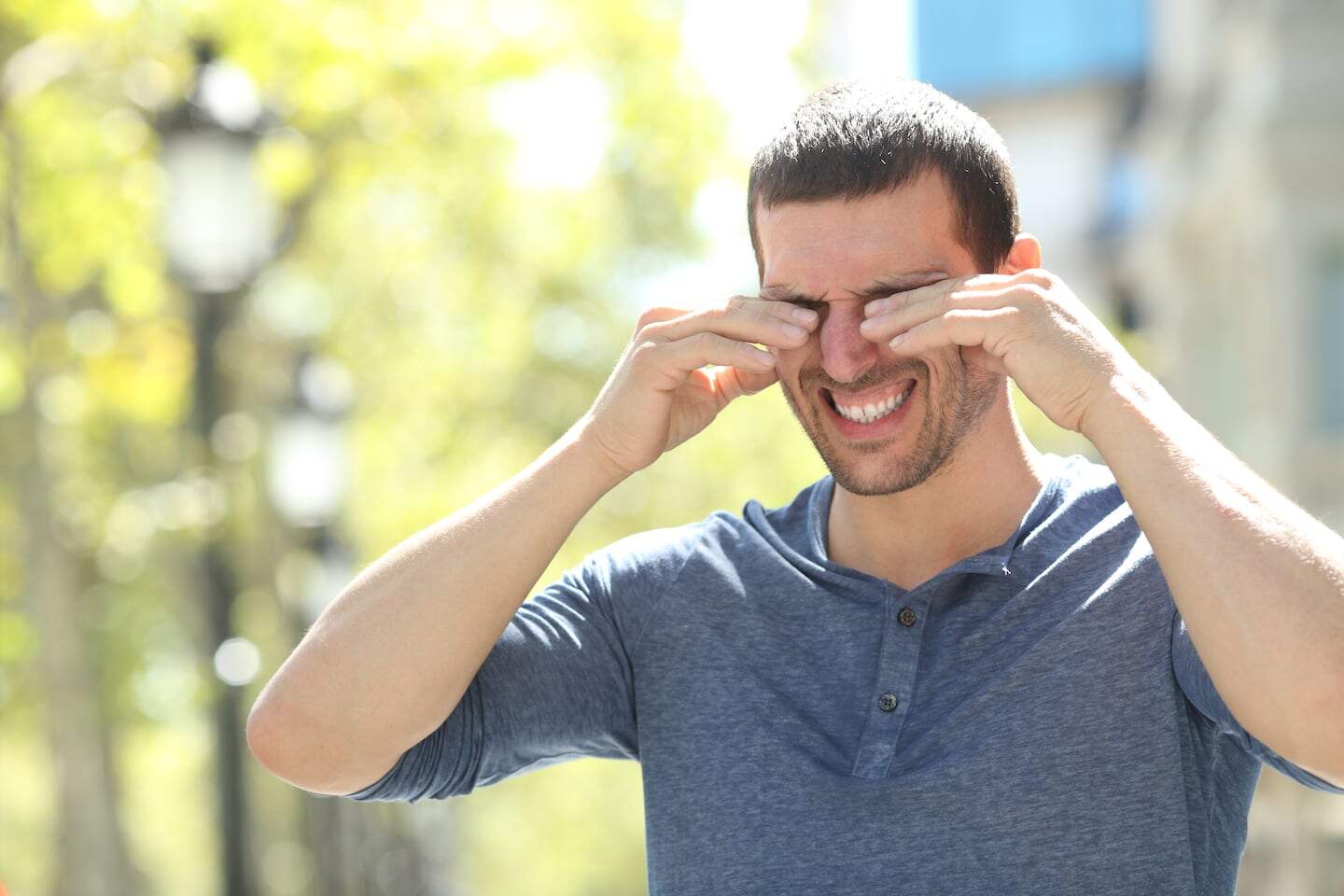 Hombre con síntomas de alergia frotándose los ojos en la calle